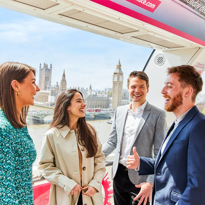 A group of four people talking inside a London Eye Pod Capsule. With a clear view of Big Ben and the Houses of Parliament in the the background.