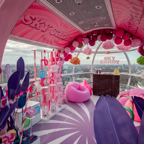 London Eye Pod Capsule decorated in different pink and purple tones. With props of sweets and signs in pink reading the sky candy emporium.