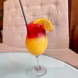 Close up of a red and orange cocktail garnished with an orange slice and served with a straw, at the Eye Lounge Bar at the London Eye